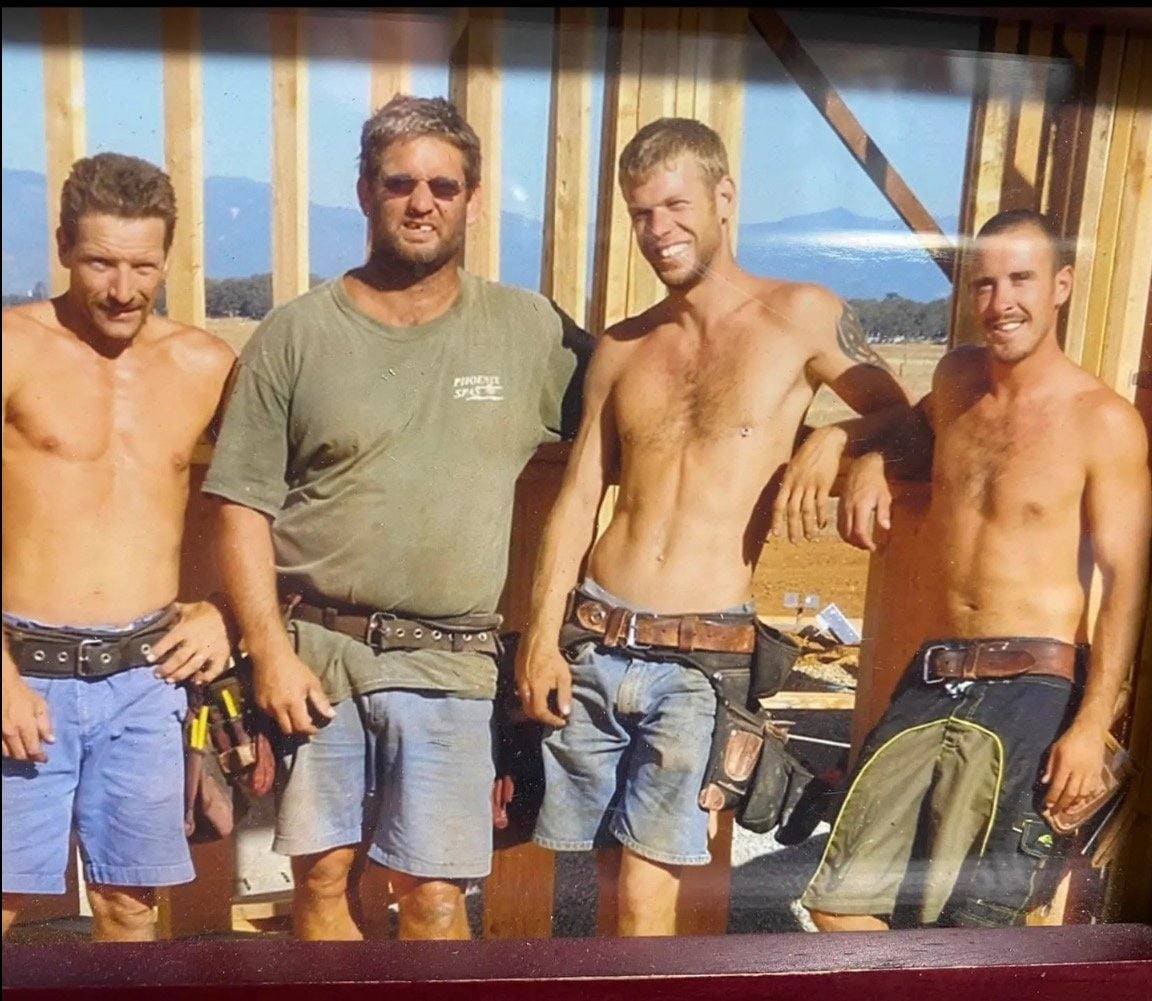 Four men posing together indoors with mountains and water visible through windows behind them