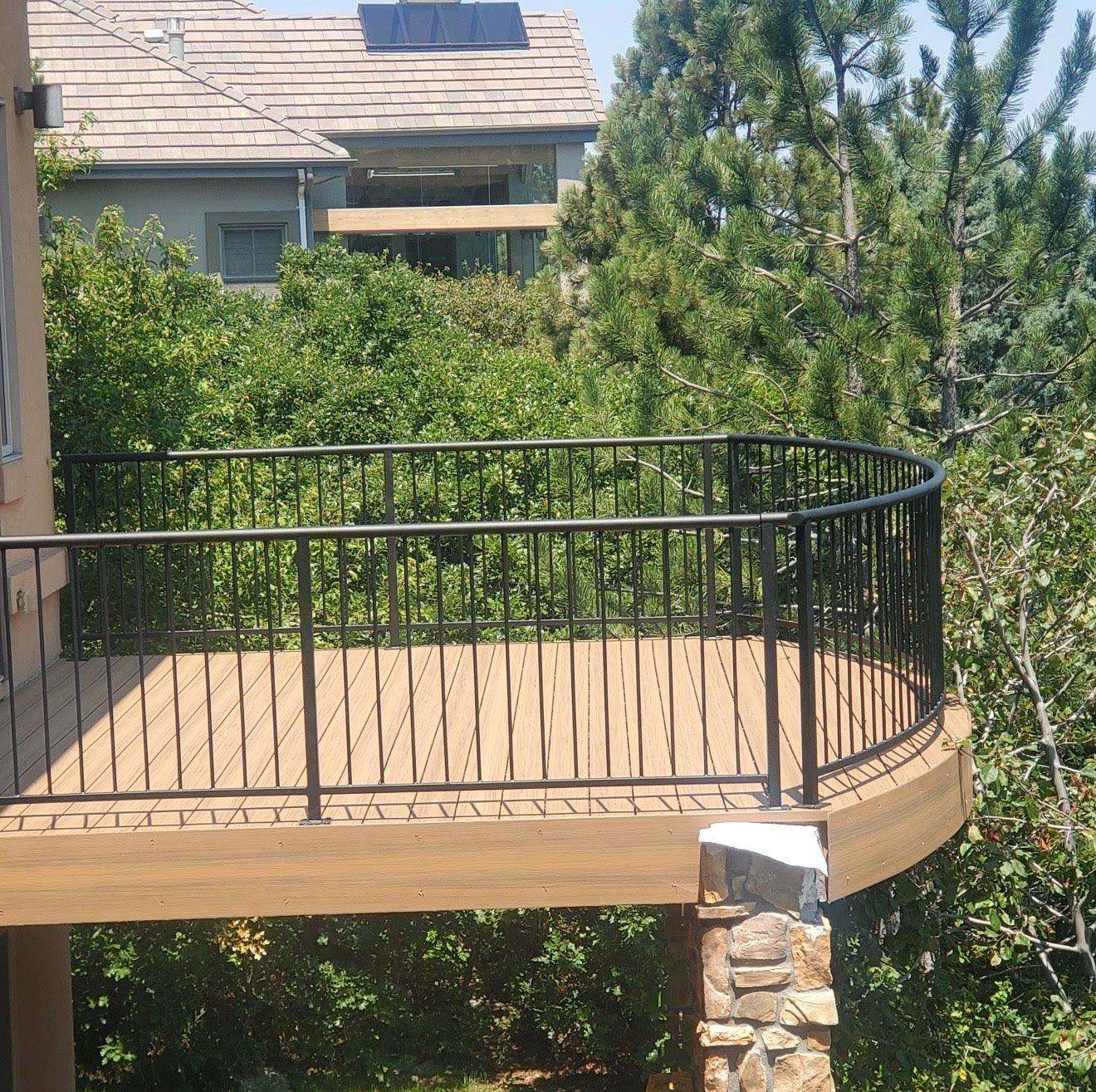 Curved wooden deck with black metal railing overlooking landscaped hillside garden
