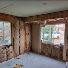 Interior renovation in progress showing exposed wooden studs, drywall, and windows in an unfinished room