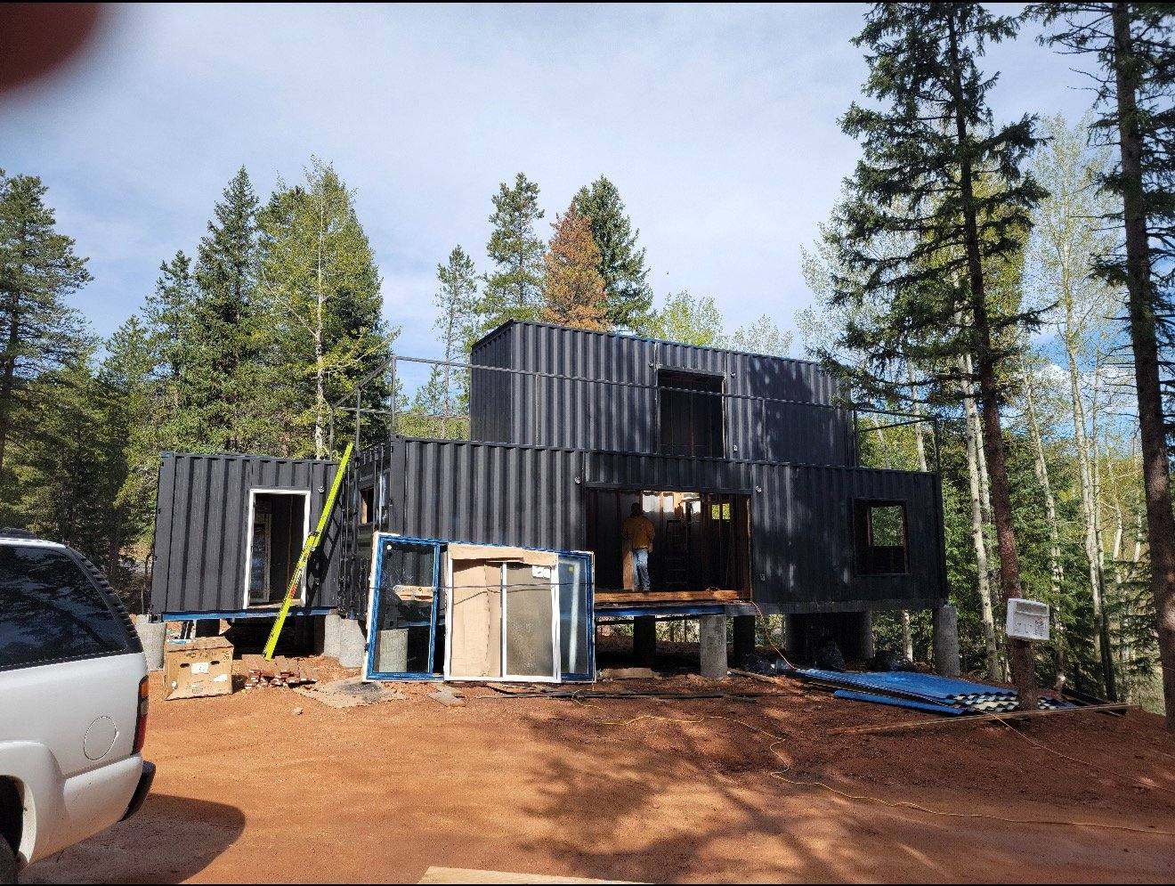 Modern black corrugated metal residential building under construction surrounded by pine trees