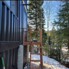 Modern dark building with wooden deck structure overlooking snowy forest landscape