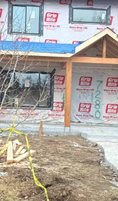 New home construction with framing, blue roof wrap, and red building permits on exterior walls