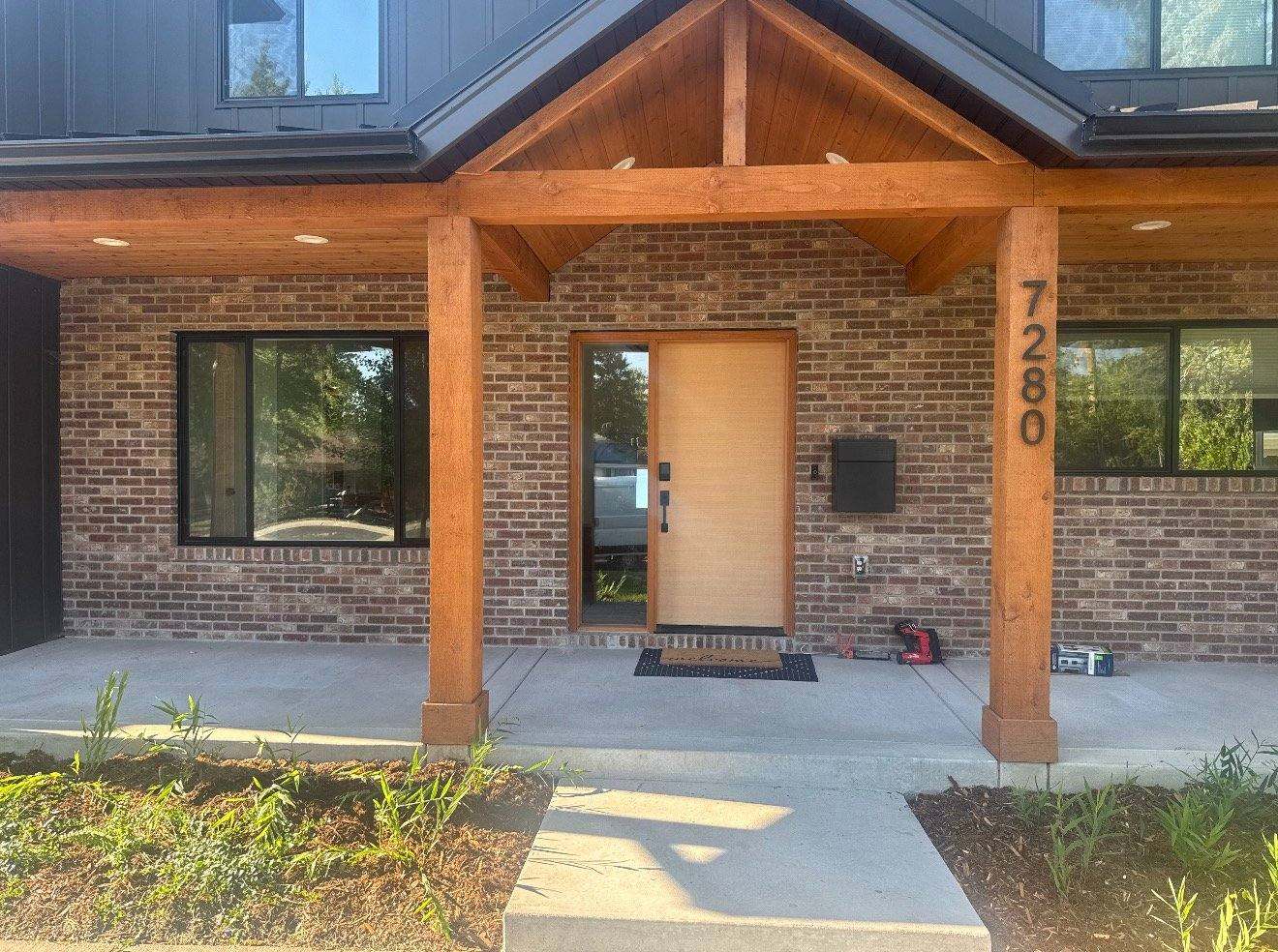 Modern brick home entrance with wooden pergola, large windows, and house number 7280