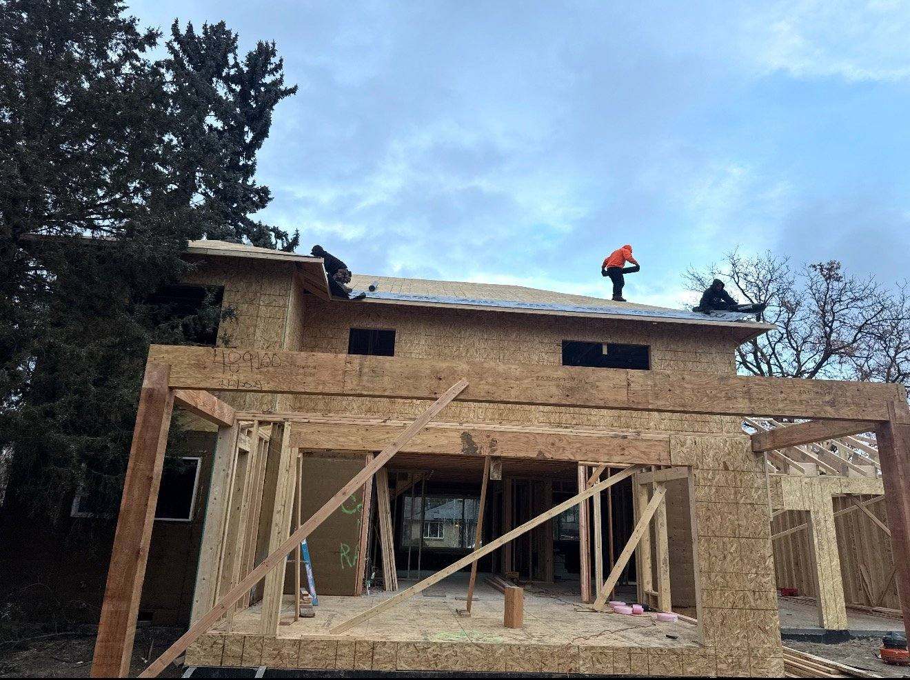 Construction workers installing roofing on wooden framed two-story house under construction