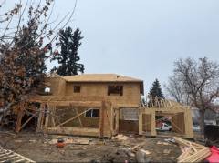 Two-story yellow house under construction with exposed framing and bare trees